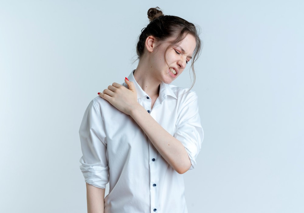Woman holding her shoulder in pain from frozen shoulder.