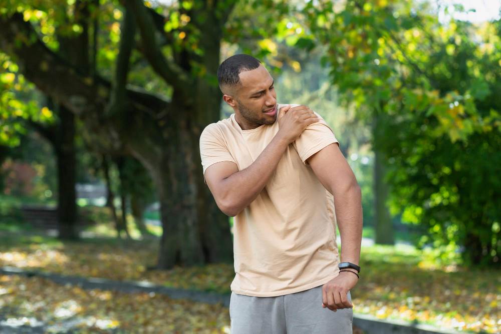 Man outdoors rubbing his shoulder from frozen shoulder stiffness.
